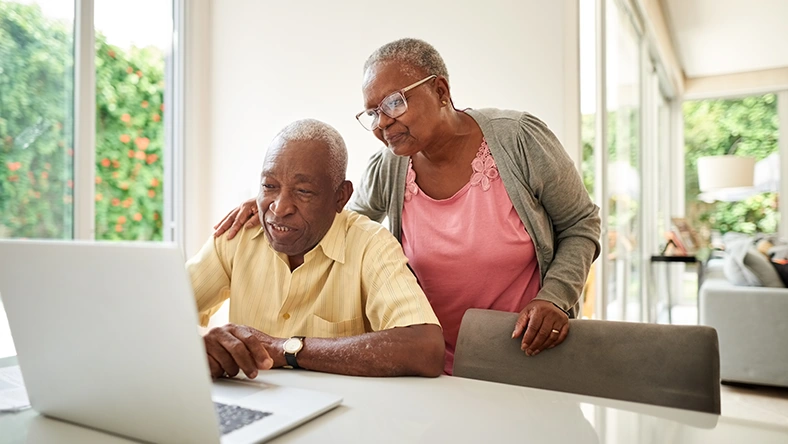 Two older adults reviewing information on a laptop at home, representing planning for Medicare coverage and retirement healthcare decisions.