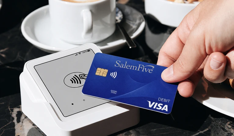 Salem Five Visa debit card being tapped on a contactless payment terminal at a café.