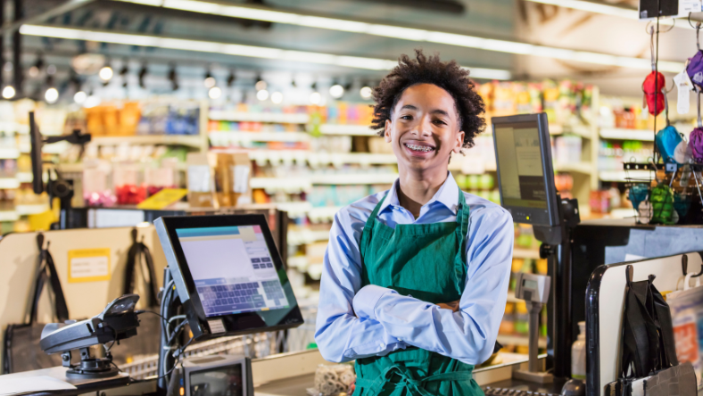 Young teen boy cashier smiling at work.