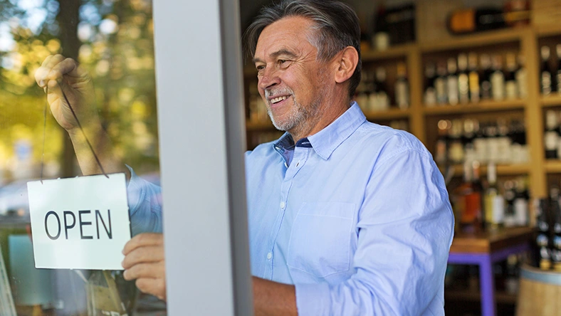 Small business owner hanging an open sign in a storefront window, representing self-employed work and income responsibility.