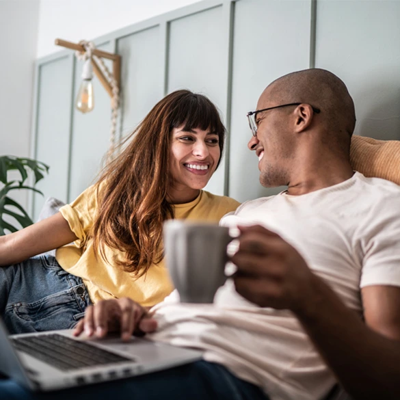 Two people sitting at home using a laptop and reviewing finances together while enjoying coffee.