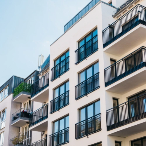 Modern apartment building exterior with black metal balconies and large glass windows against a clear sky.