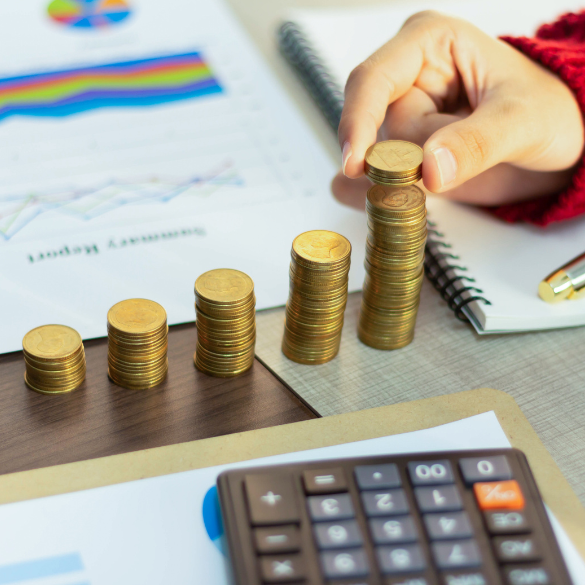 Hand stacking coins on work desk with charts and calculator.