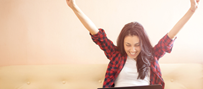 Woman raising arms in excitement looking down at laptop.